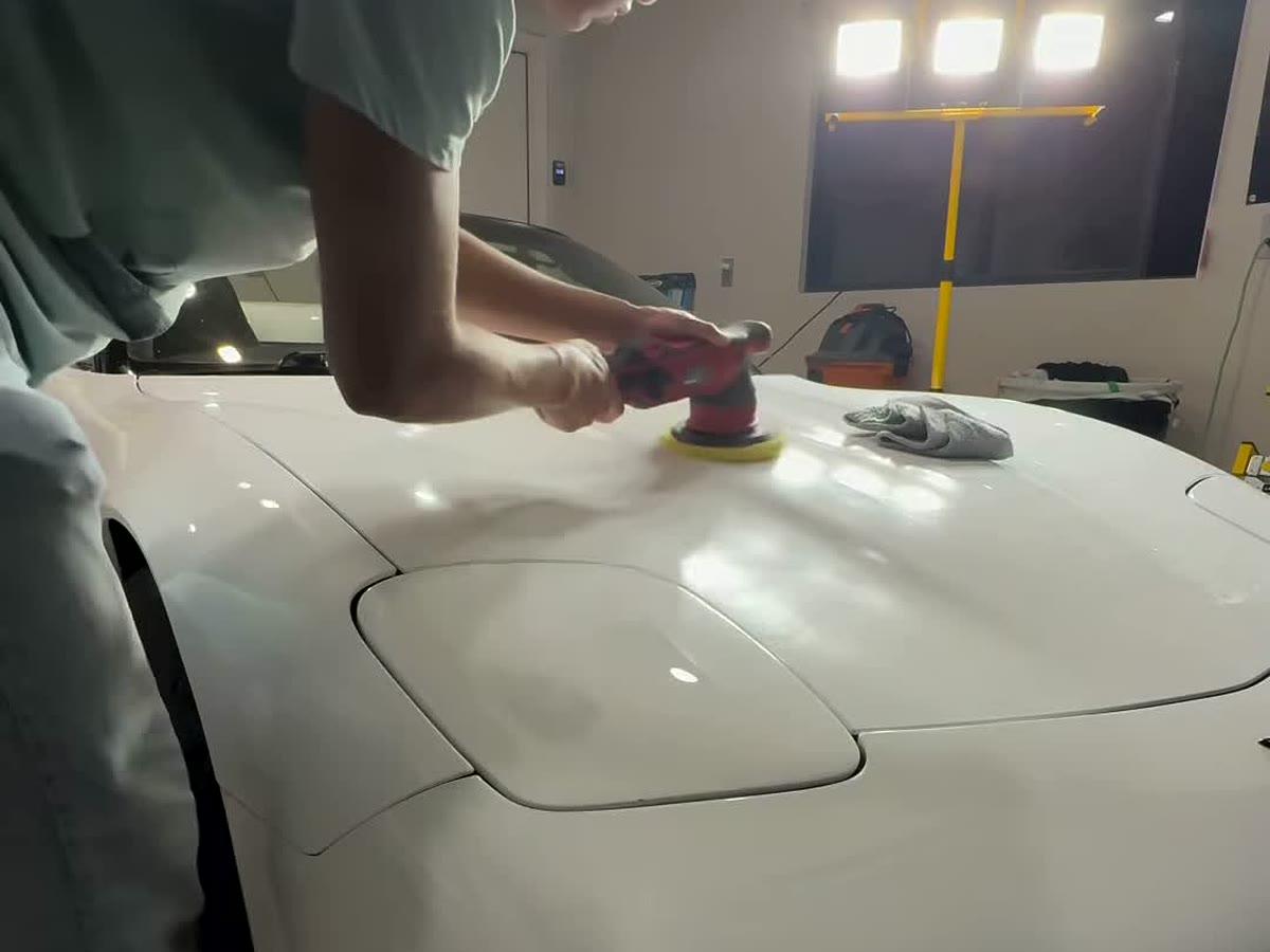 Machine-polishing the hood of a white Corvette under work lights