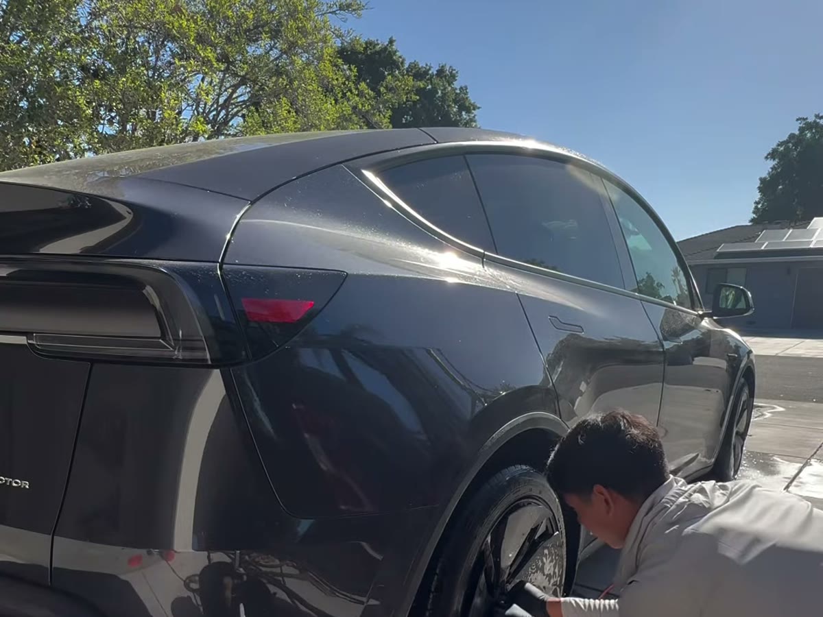 Detailing the rear wheel of a glossy black Lucid Air with a wheel brush